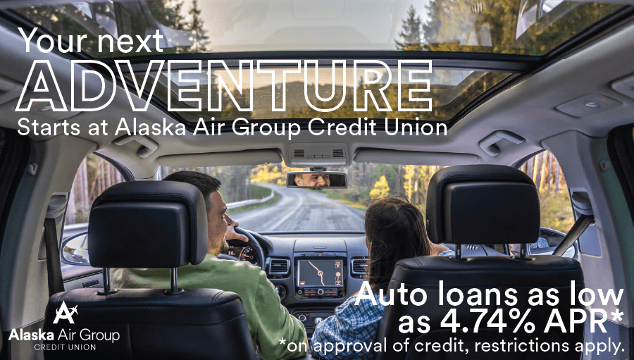 A couple drives down a scenic road, overlaid text reads "Your next adventure starts at Alaska Air Group Credit Union. Auto loans as low as 4.74% APR* *On approval of credit, restrictions apply." 